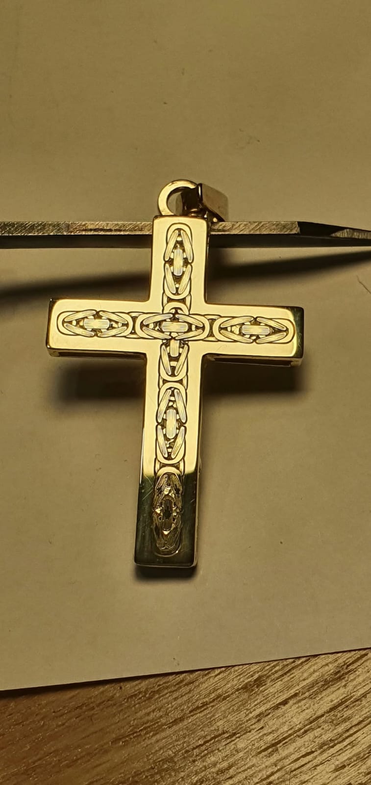 Zlat križni obesek s pletenim ornamentom po krakih.