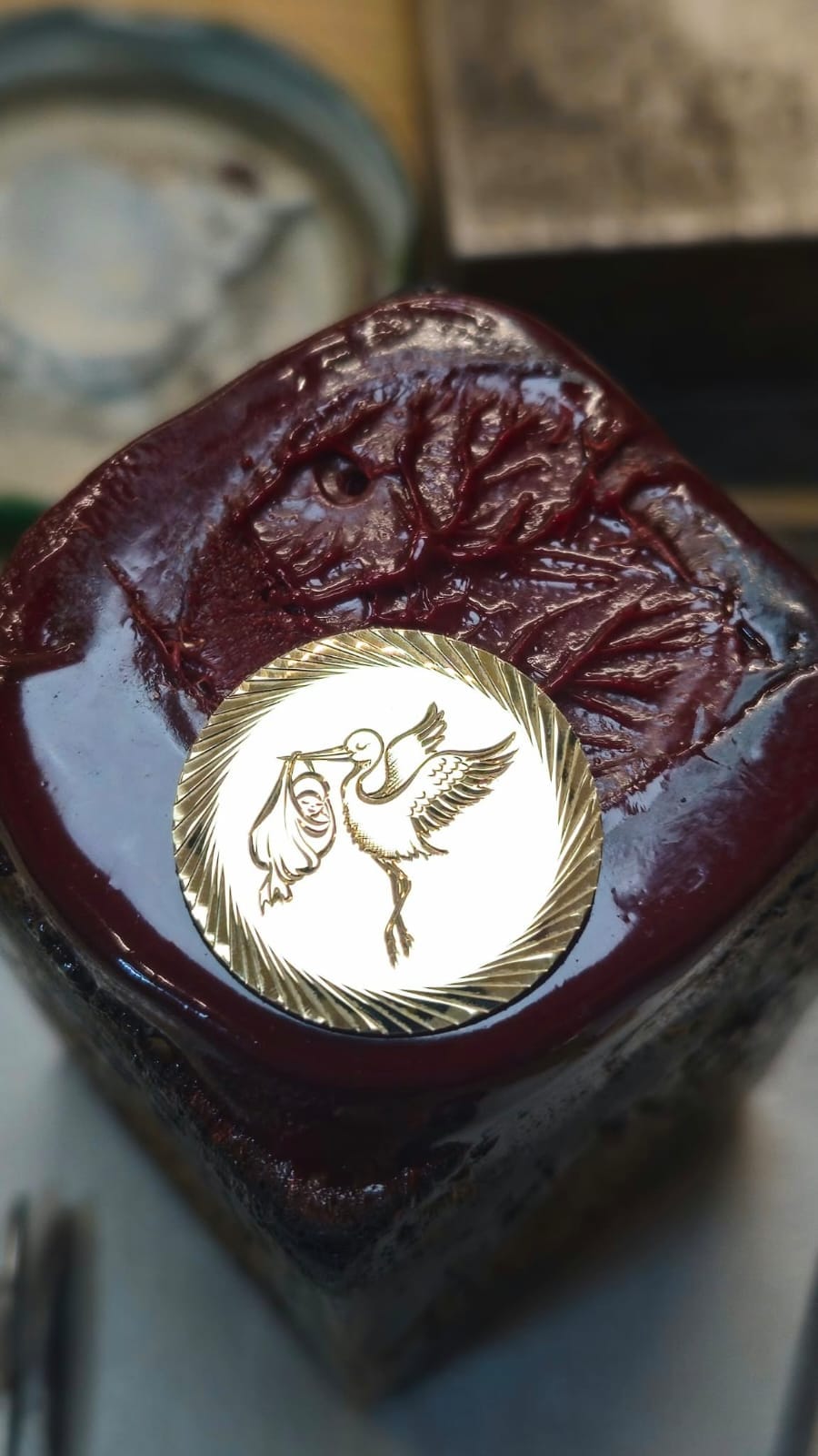 Zlat okrogel medaljon z gravirano štorkljo, ki nosi povitek.