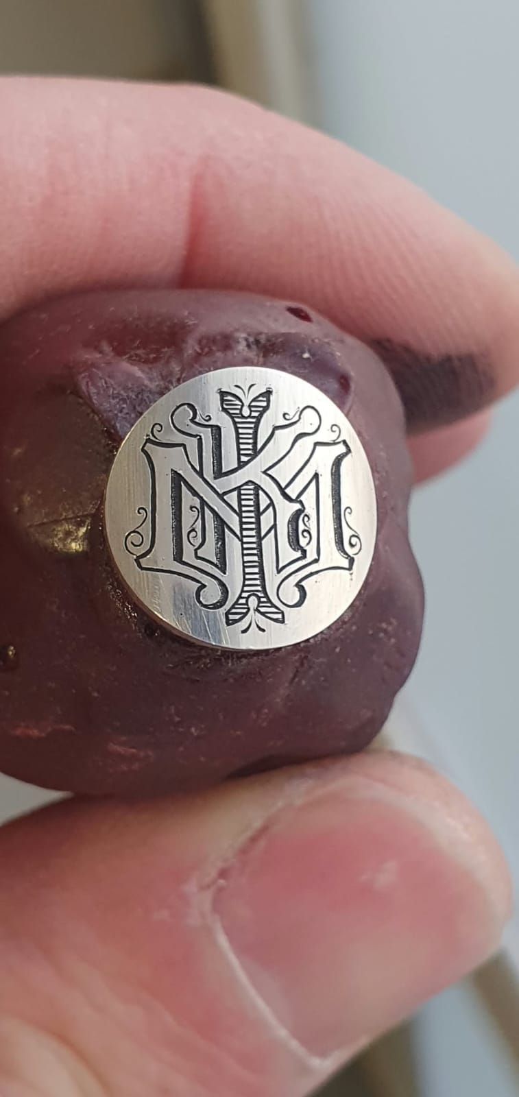 Okrogla srebrna ploščica z bogato okrašenim monogramom.