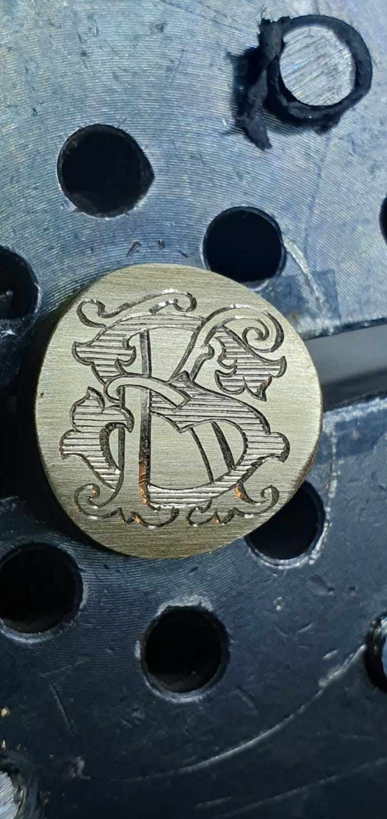 Okrogla medeninasta ploščica z vgraviranim prepletenim monogramom.