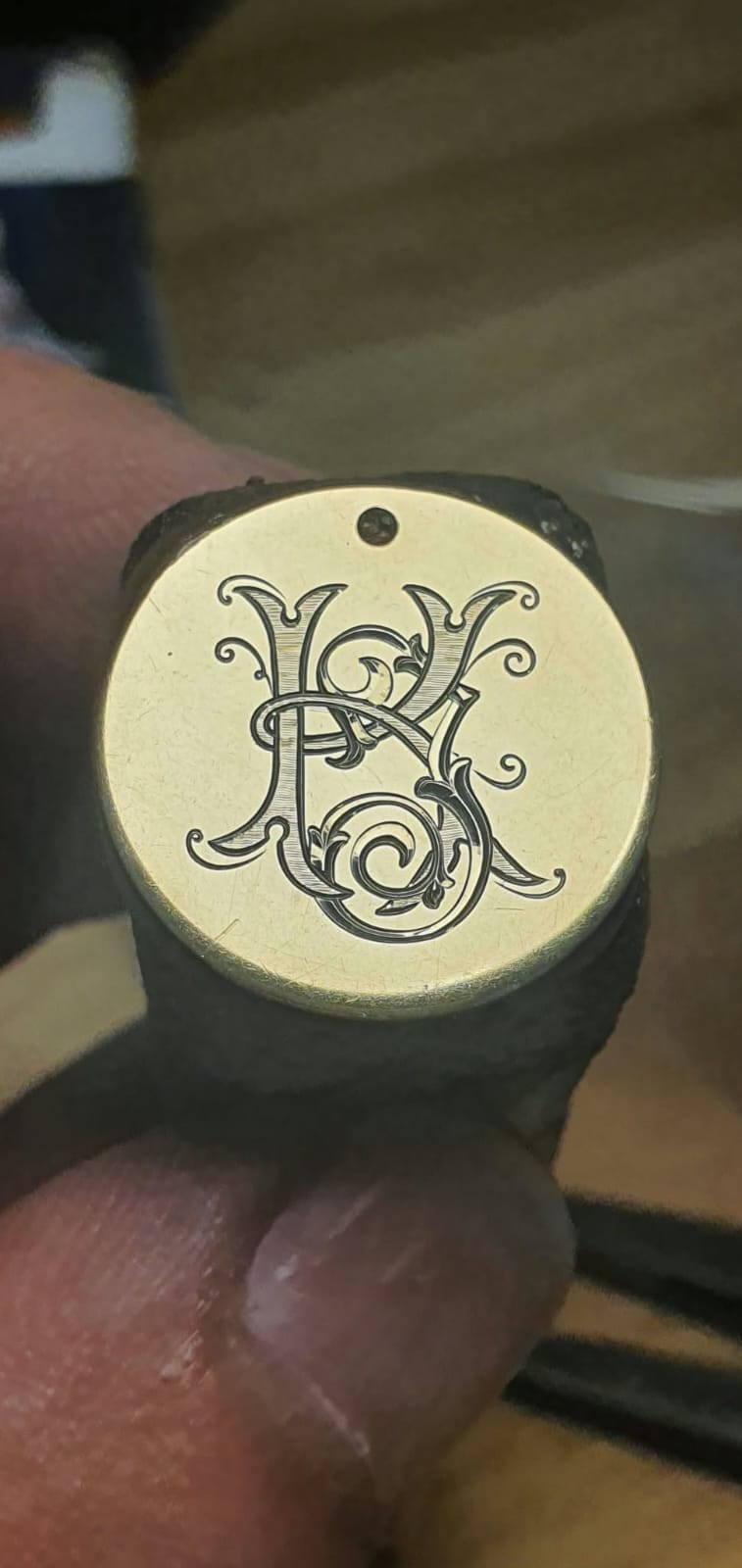 Zlata okrogla ploščica z ročno graviranim prepletenim monogramom.