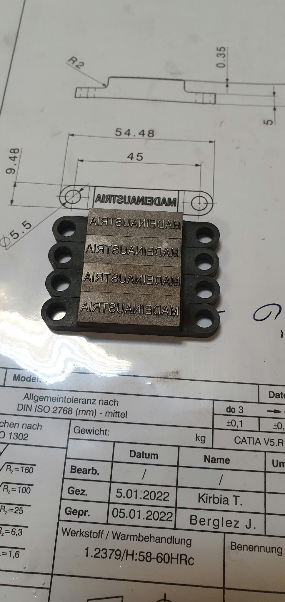 Kovinske ploščice z vgraviranim napisom na tehnični risbi.