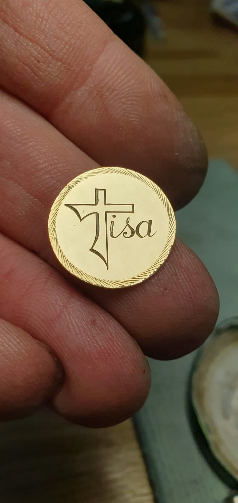 Okrogla zlata ploščica s križem in žarkastim robom.