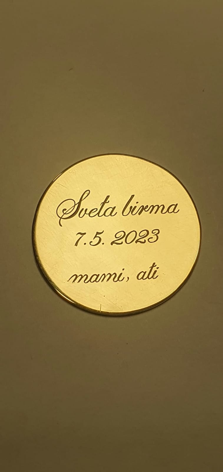 Okrogla zlata ploščica z vgraviranim posvetilom in datumom.